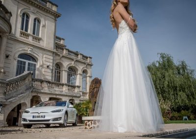 Focus sur la robe de la mariée, avec une Tesla S blanche en fond